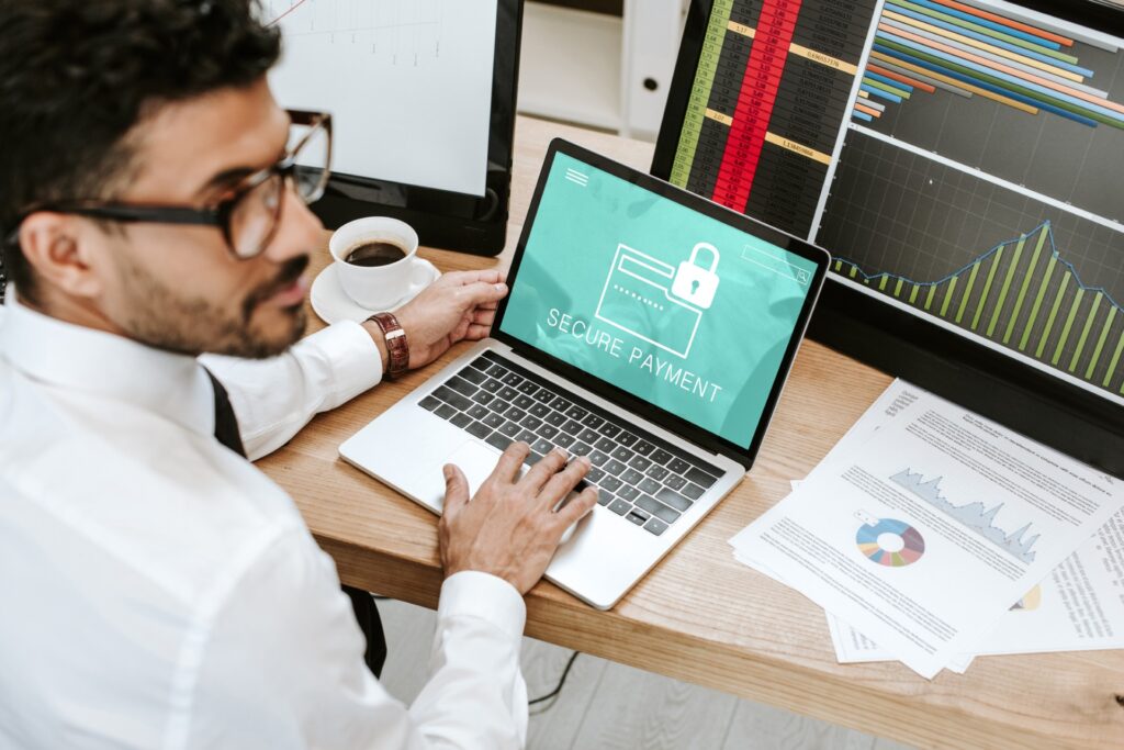 Mann mit Hemd und Brille vor Diagrammen und Laptop mit Fokus auf ‚Secure Payment
